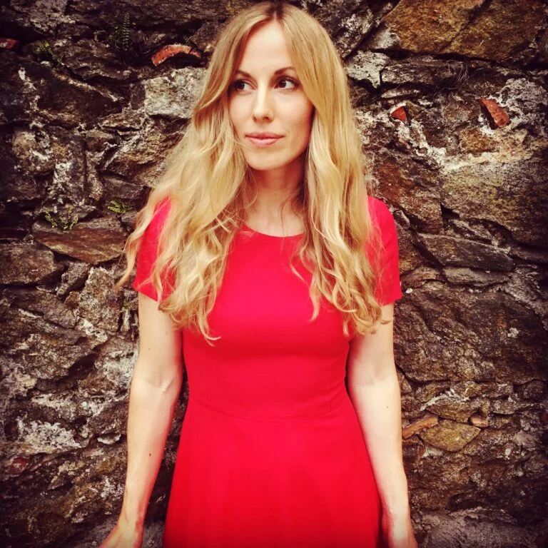 Die Sängerin Vera Klima mit langen blonden Haaren und rotem Kleid vor einer alten Steinmauer, August 2017.
